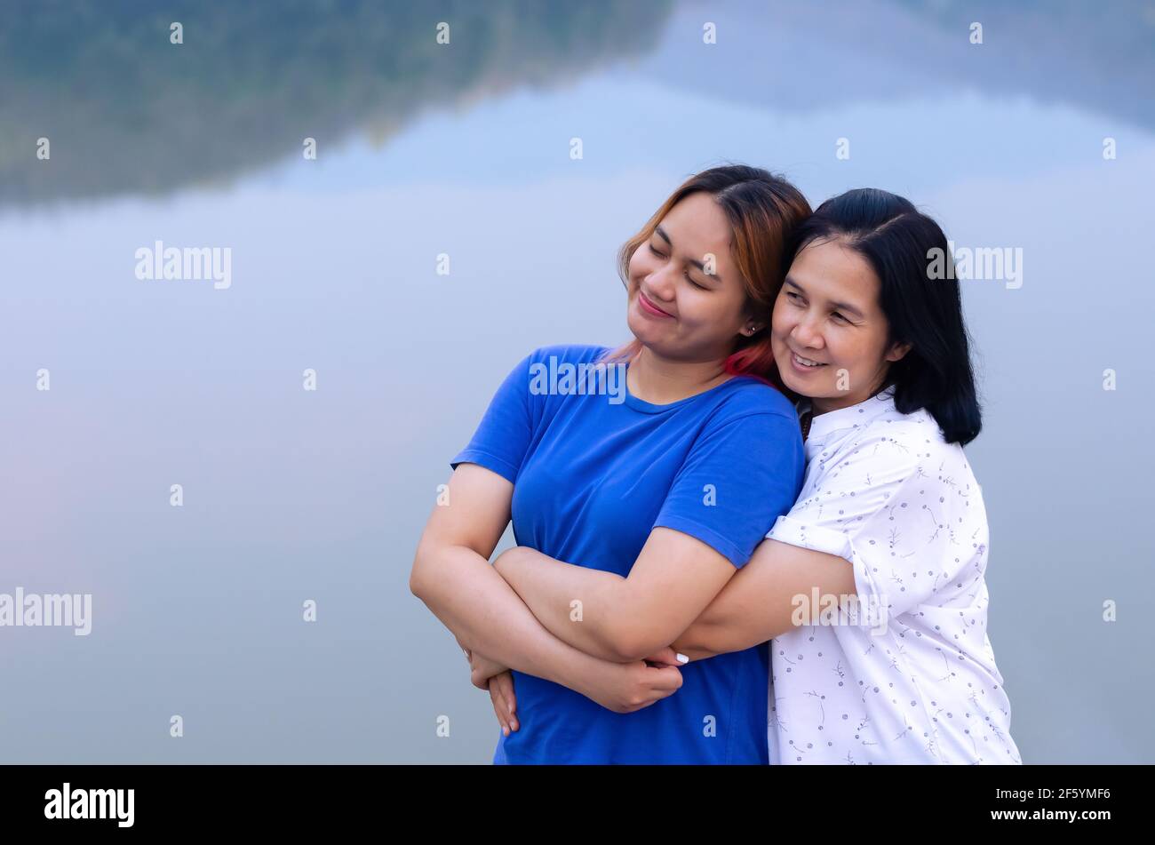 Madre asiatica singola e la sua figlia adolescente abbracciano insieme sullo sfondo del lago con l'ombra di montagna. Concetto di giorno della madre Foto Stock