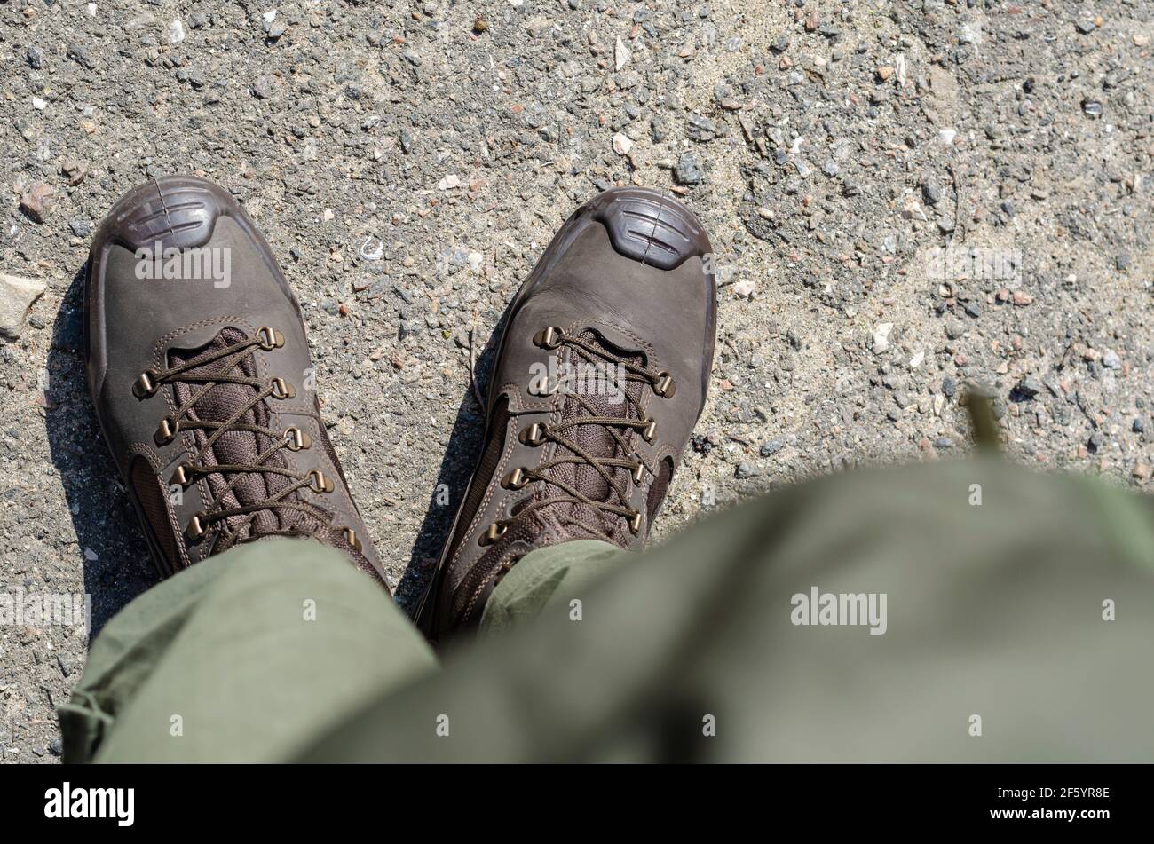 Gambe in stivali militari marroni e pantaloni verdi. Soldato in piedi in uniforme sulla pavimentazione esterna. Vista dall'alto in un angolo. Foto Stock