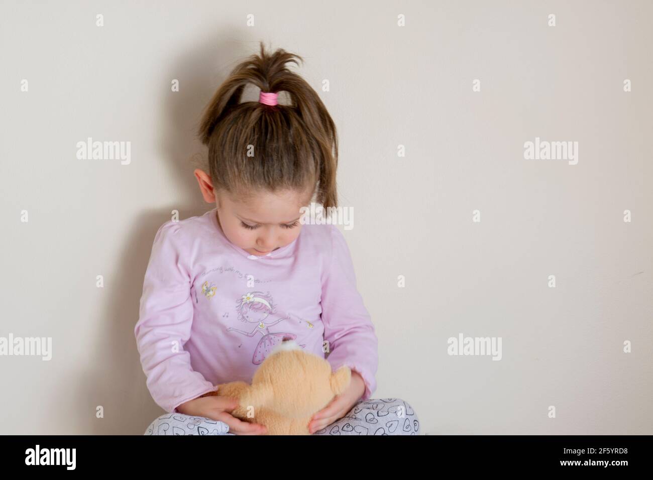 chubby piccola ragazza gioca con il suo orsacchiotto mentre attende il suo esame pediatrico. Volto fuoco selettivo Foto Stock