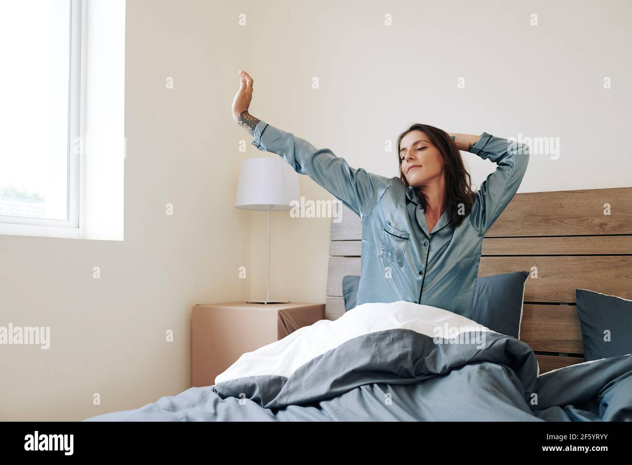Bella giovane donna in pigiama di seta che si allunga a letto dopo svegliarsi al mattino Foto Stock