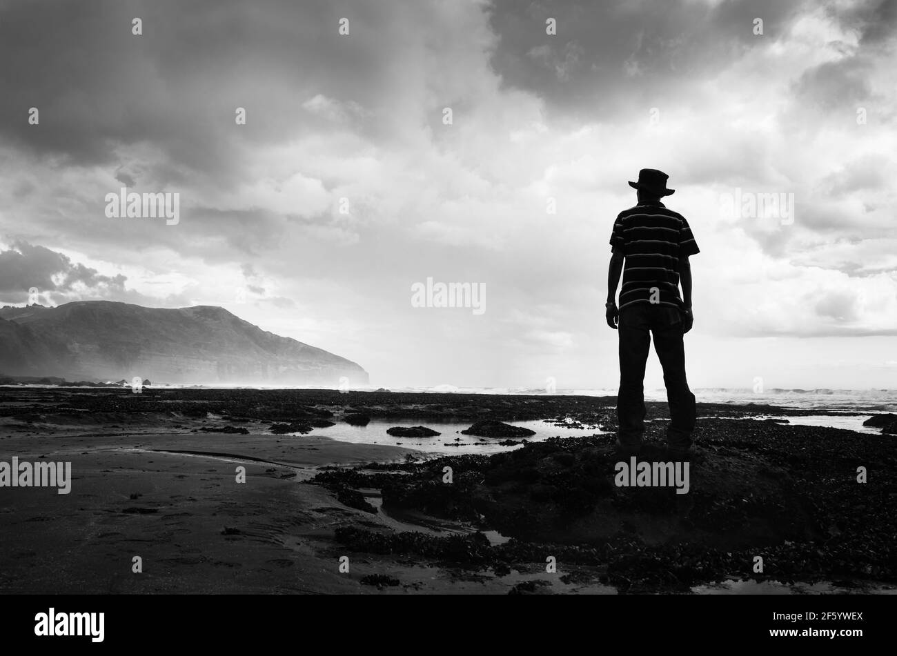 Immagine in bianco e nero di un uomo che si trova sulle rocce e guarda la tempesta che si avvicina alla spiaggia di Muriwai, ad ovest di Auckland Foto Stock Immagine in bianco e nero di un uomo che si trova sulle rocce e guarda la tempesta che si avvicina alla spiaggia di Muriwai, ad ovest di Auckland Foto Stock
