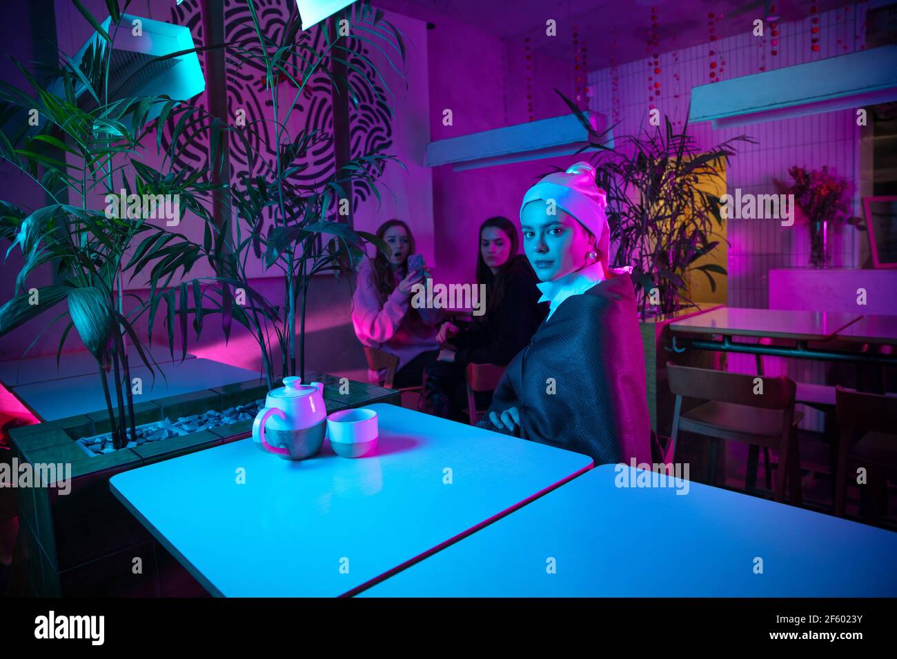 Bella ragazza con un orecchino perla che pranza in un moderno cafe, ristorante in luce al neon Foto Stock