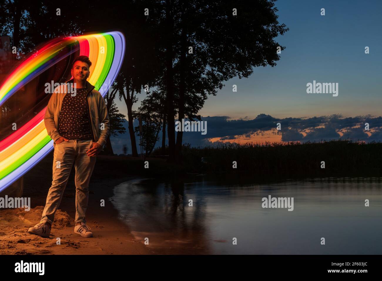 giovane uomo in piedi su una spiaggia di sabbia del lago con calma rainbow luce astratta dietro di lui Foto Stock