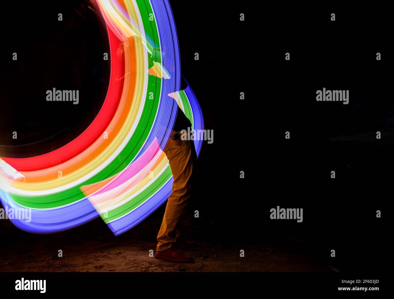 silhouette giovane uomo in piedi su uno sfondo scuro con arcobaleno disegno tramite luce di congelamento Foto Stock