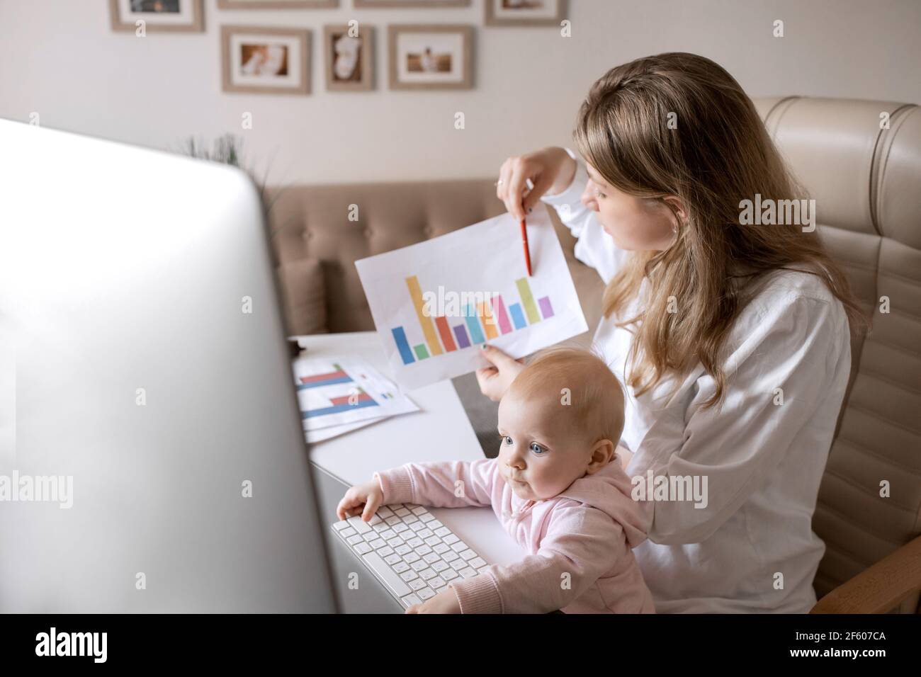 La giovane madre sta lavorando in modo distante a casa mentre baby figlia piccola, avendo conferenza in linea. Dipendente femminile concentrato che discute con Foto Stock
