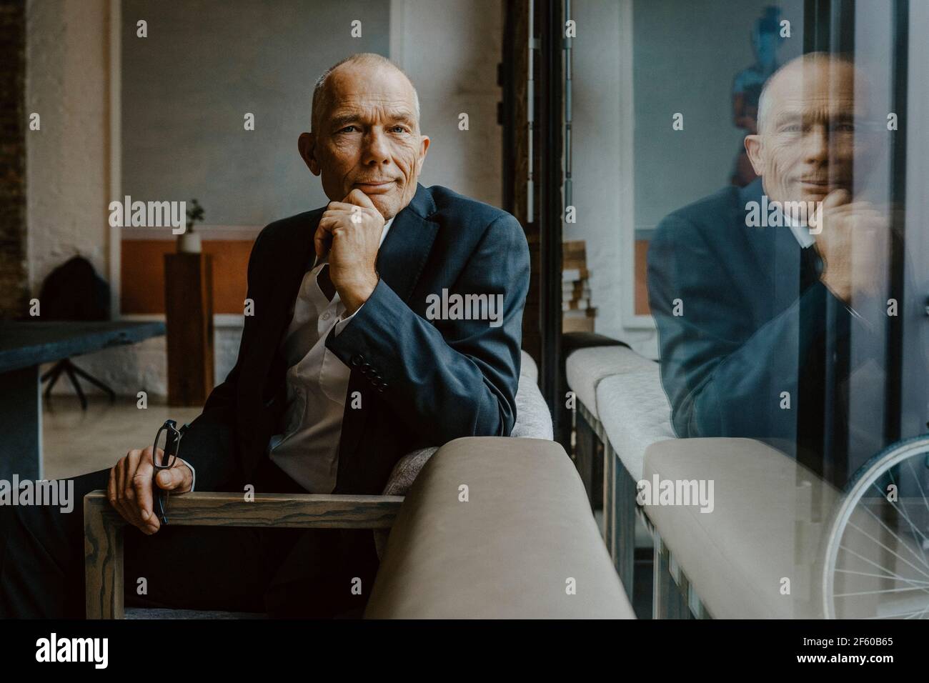 Ritratto di uomo d'affari con la mano sul mento seduto sul divano in ufficio Foto Stock