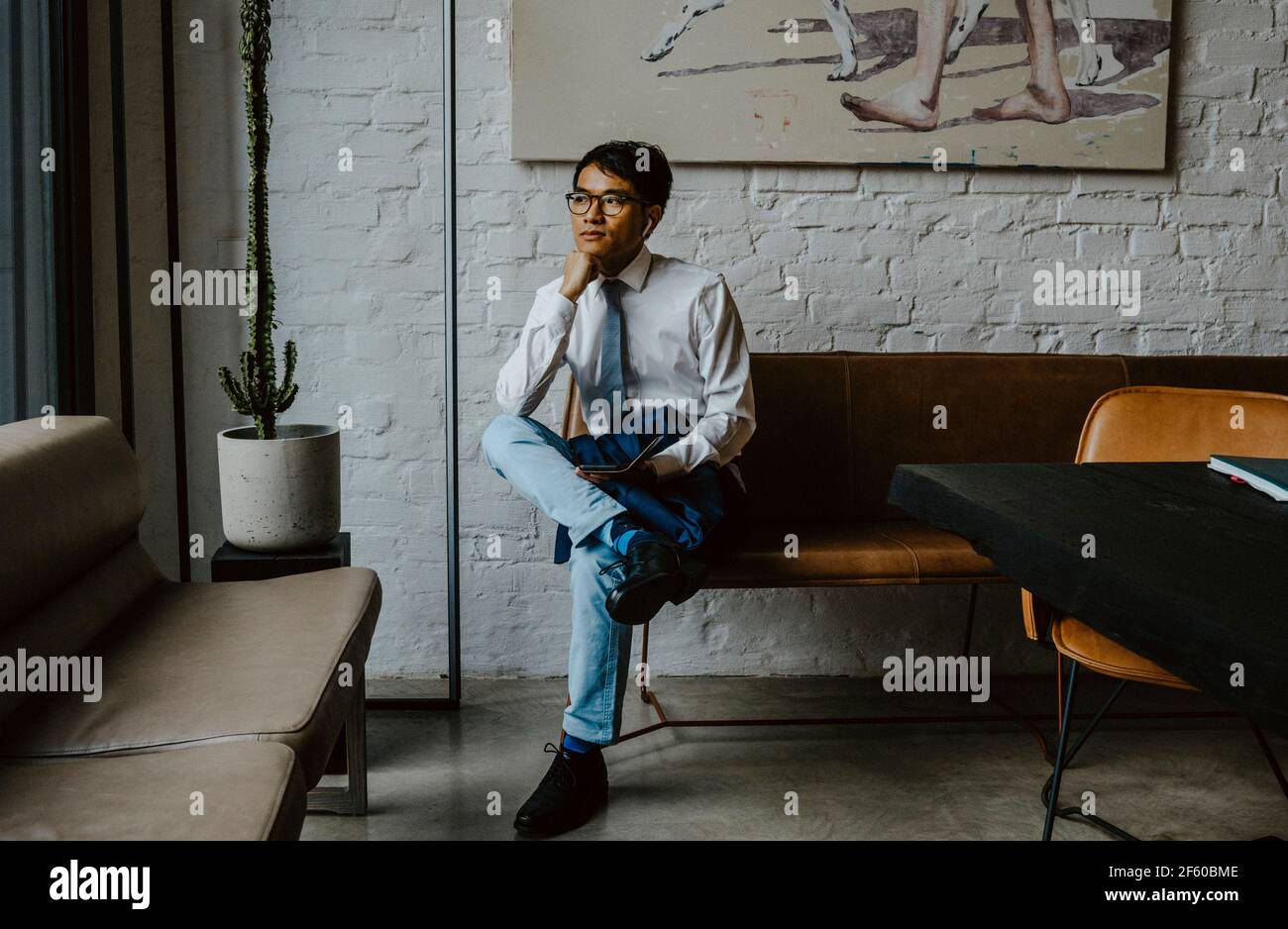 Uomo d'affari seduto sul divano con la mano sul mento in ufficio Foto Stock