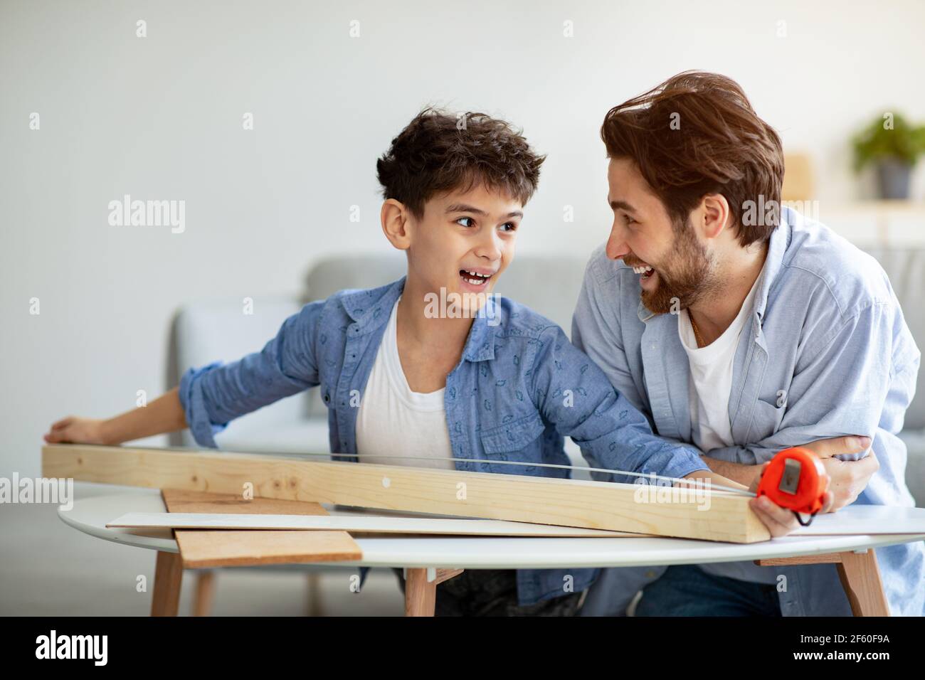 Miglior team. Allegro padre e figlio che misura la tavola di legno con nastro. Casa per la produzione di uccelli in famiglia con dettagli in legno Foto Stock