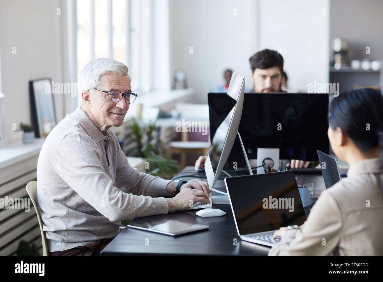 Ritratto di sorridente anziano che collabora con i giovani in ufficio moderno, concetto di cambiamento di carriera, spazio di copia Foto Stock