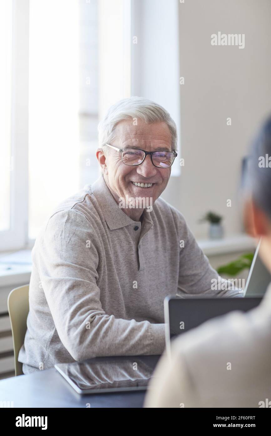 Ritratto verticale di sorridente anziano che collabora con i giovani in ufficio moderno, concetto di cambiamento di carriera Foto Stock