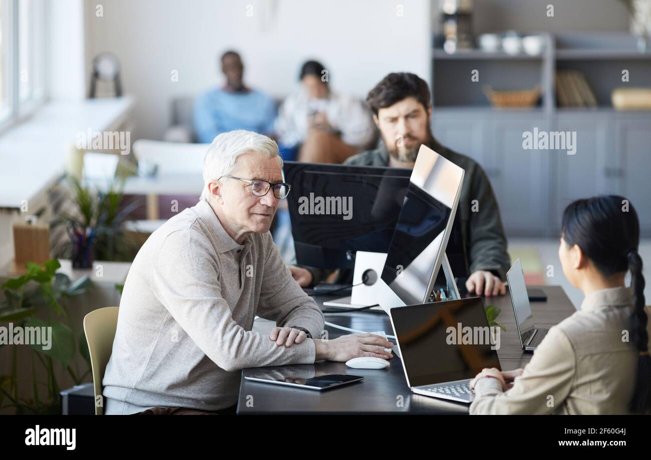 Ritratto di un anziano dai capelli bianchi che collabora con i giovani in un ufficio moderno, concetto di cambiamento di carriera, spazio di copia Foto Stock