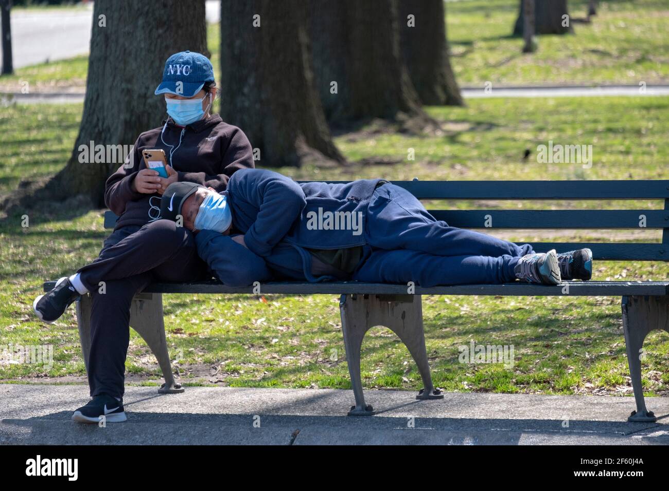 Una coppia su una panchina di parco in Flushing prati Corona Park. Sta dormendo in grembo e sta leggendo dal suo telefono cellulare. Foto Stock