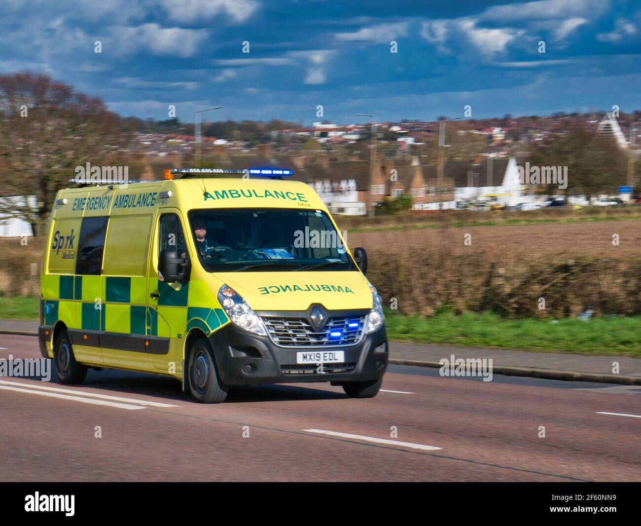 Un'ambulanza NHS che viaggia ad alta velocità su una strada in un'area semi-urbana dell'Inghilterra, Regno Unito. In una giornata luminosa e soleggiata con un cielo blu in primavera. Foto Stock