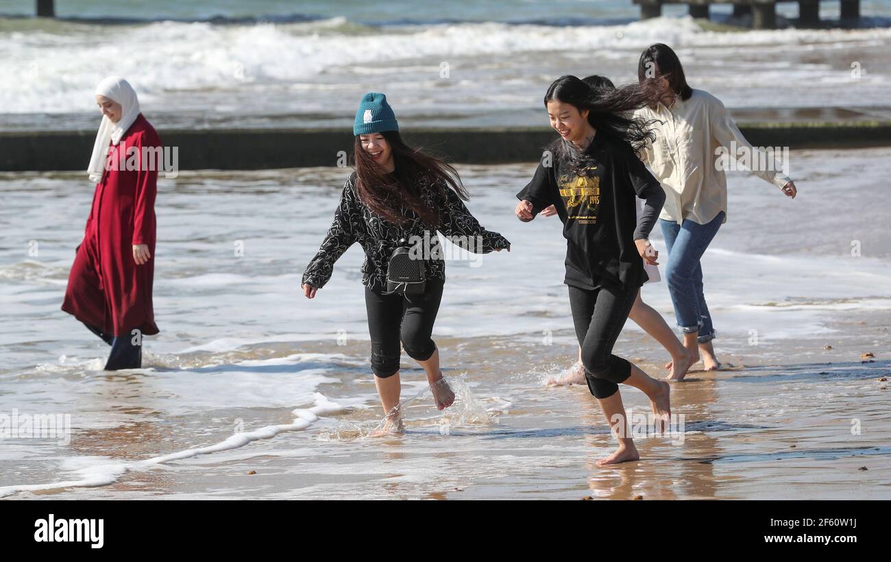 Bournemouth, Regno Unito. 29 marzo 2021. Un gruppo di studenti cinesi di Birmingham si divertono nel caldo sole di marzo per visitare la spiaggia di Bournemouth per la giornata del primo giorno di allentamento della terza chiusura nazionale Covid-19 che consente a gruppi di massimo sei amici di riunirsi in uno spazio esterno. Credit: Richard Crease/Alamy Live News Foto Stock