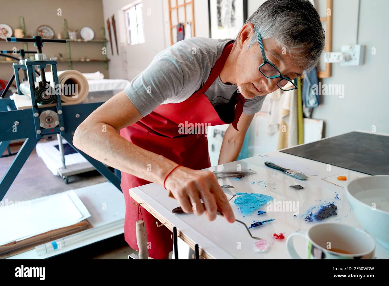 Artista che lavora nel suo studio con pennelli e una stampa Foto Stock