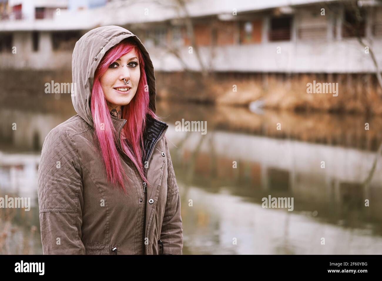 giovane donna traforata con capelli rosa e parka con cappuccio in piedi dal fiume Foto Stock