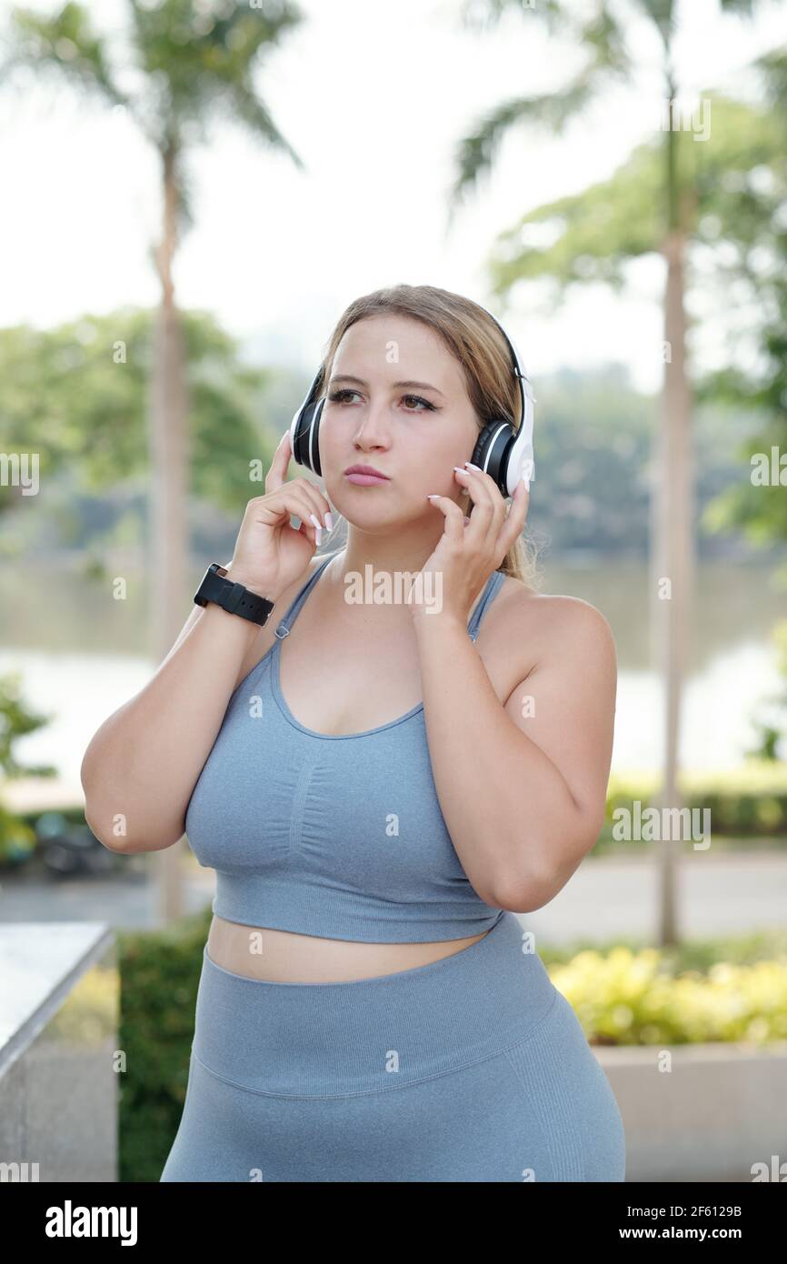 Bella vestibilità e dimensioni giovane donna che ascolta la musica in cuffie dopo un'esperienza all'aperto Foto Stock