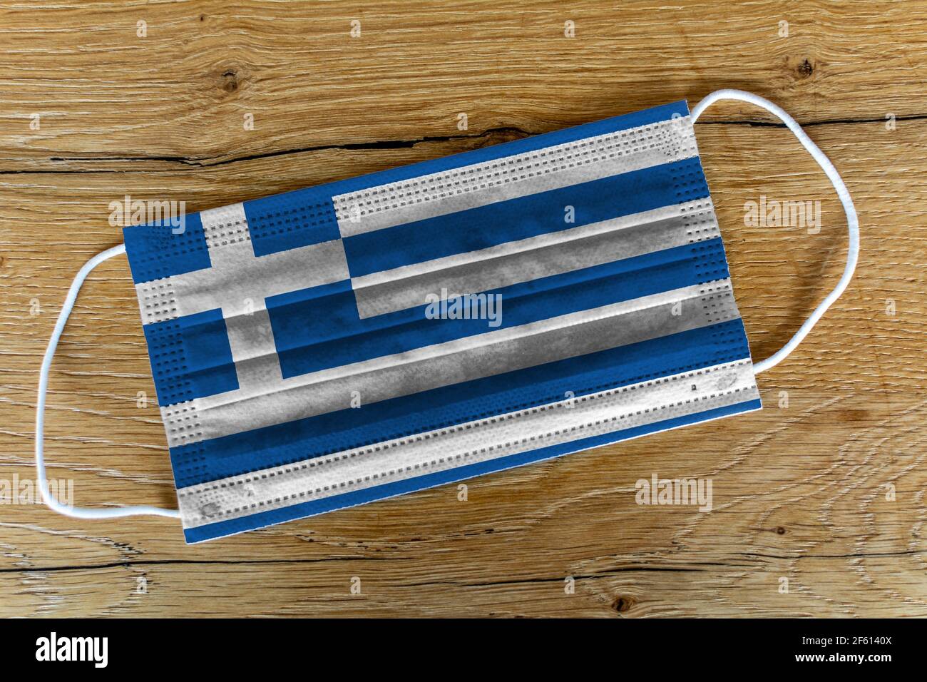 Una maschera chirurgica con la bandiera dipinta della Grecia (Repubblica ellenica) su sfondo di legno. Concetto di Grecia durante una pandemia, Covid-19, Corona Foto Stock