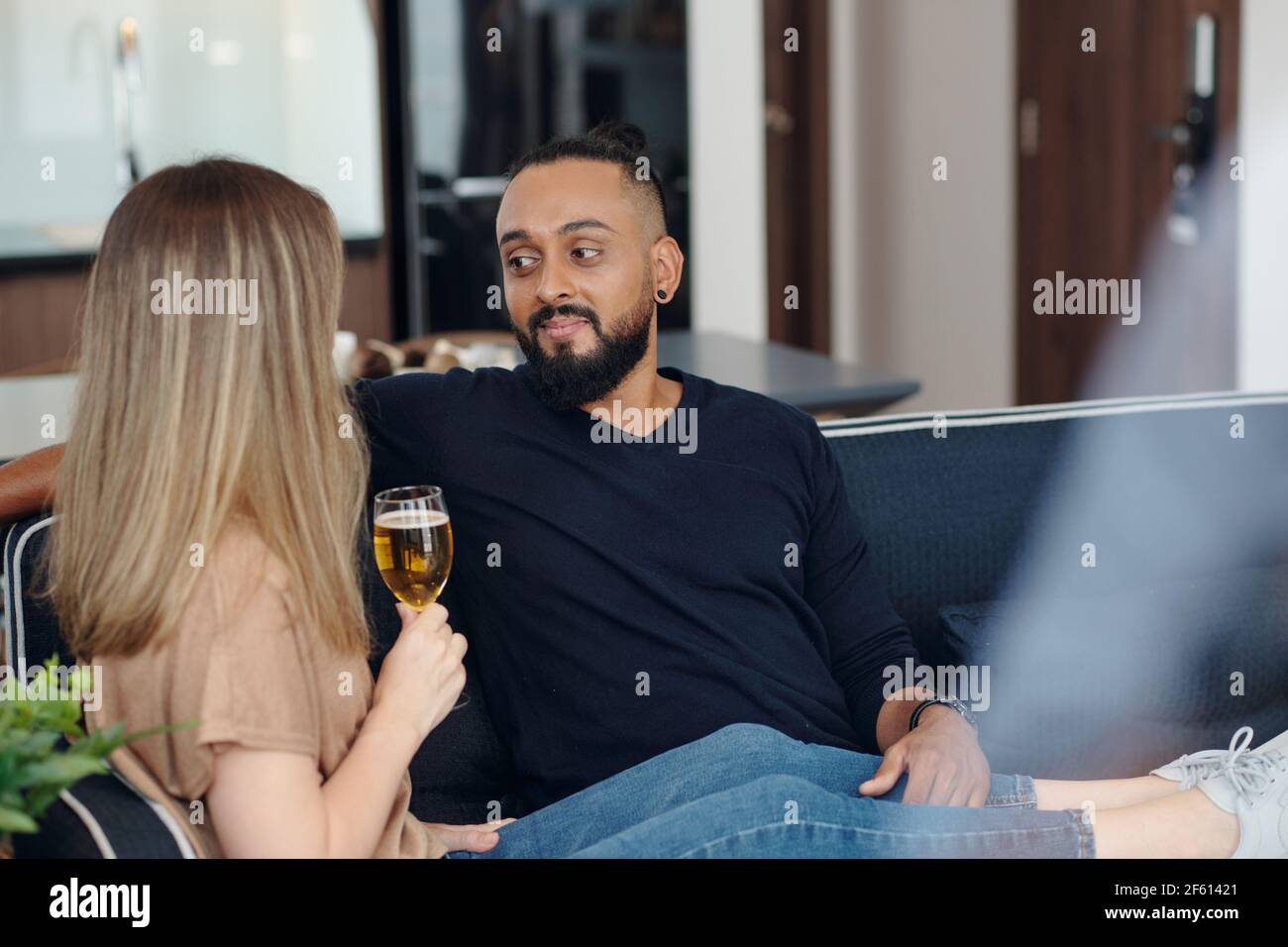 Un uomo sorridente che si riposa sul divano con la ragazza che beve champagne e raccontando il suo giorno Foto Stock
