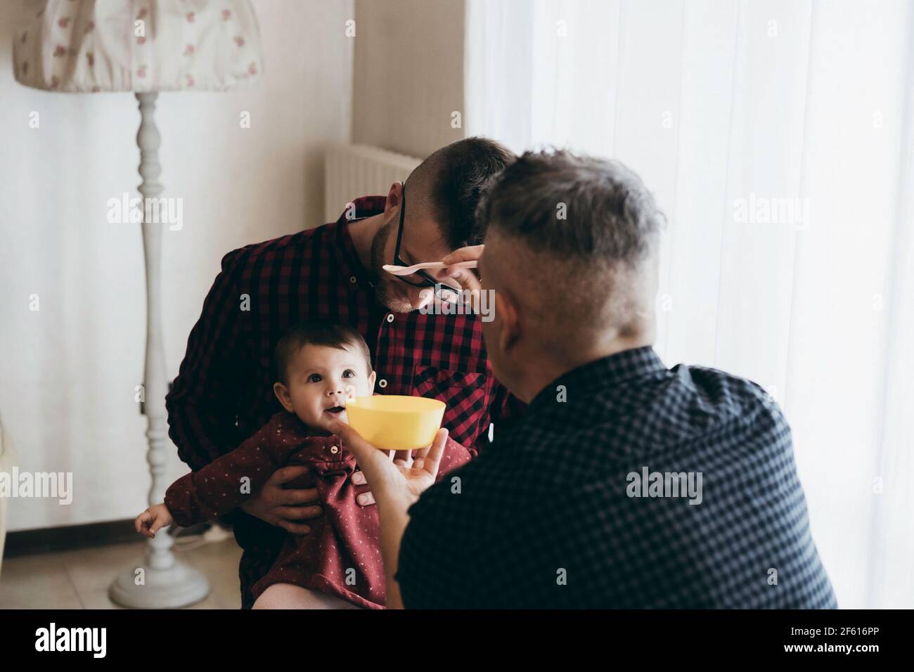 Coppia gay maschile con bambina adottata a casa - Due bei dads alimentano la ragazza del bambino sulla cucina - Babysitter maschile - la famiglia LGBT a casa - Diversity Foto Stock