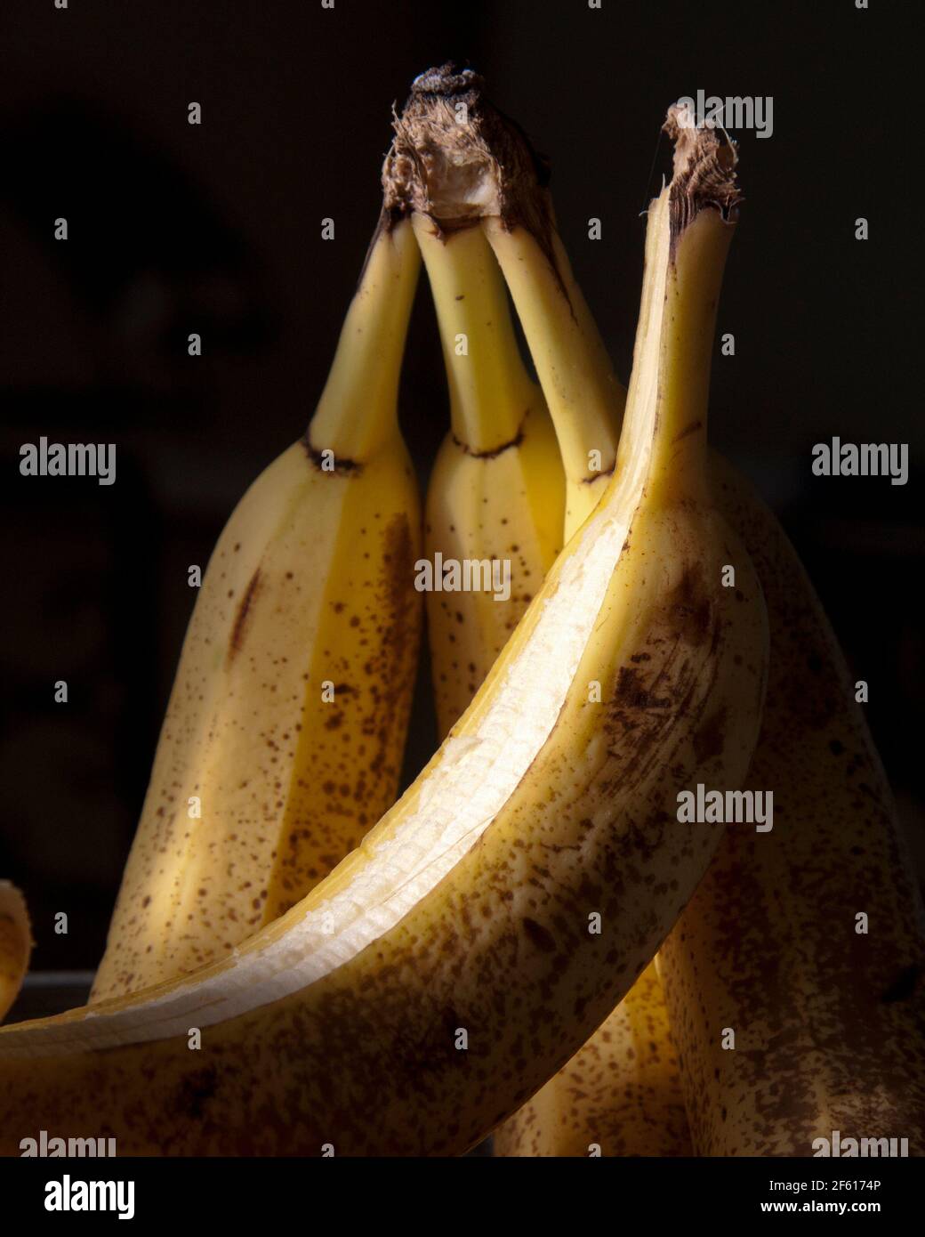 Mazzo maturo di banane gialle con macchie brune di frinckle l'illuminazione dei tasti è bassa e lo sfondo nero è ancora vivo Foto Stock