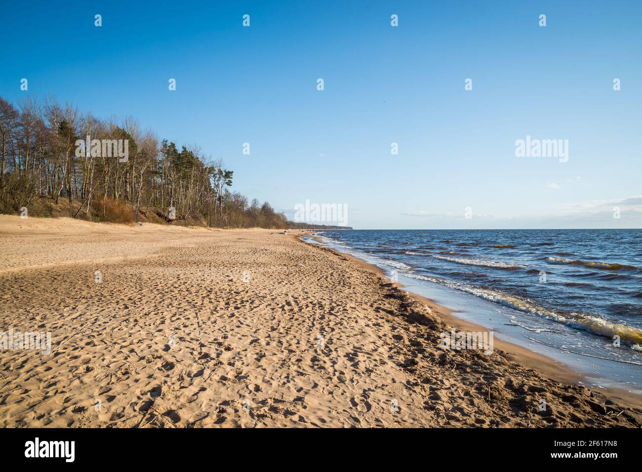 Bellissima vista mare spiaggia con cielo blu, sabbia marrone duna con impronte umane. La costa è bagnata da splendide onde di mare. Paesaggio primaverile. Foto Stock