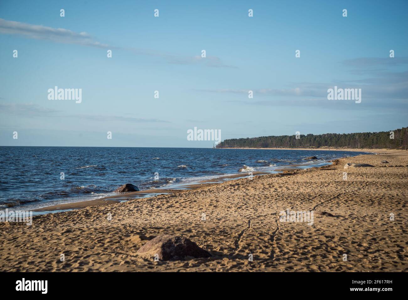 Bellissima vista mare spiaggia con cielo blu, sabbia marrone duna con impronte umane. La costa è bagnata da splendide onde di mare. Paesaggio primaverile. Foto Stock