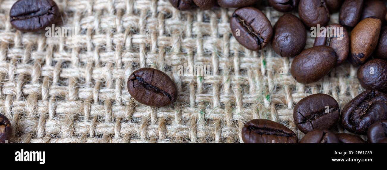 primo piano di chicchi di caffè tostati su tessuto di iuta, panorama Foto Stock