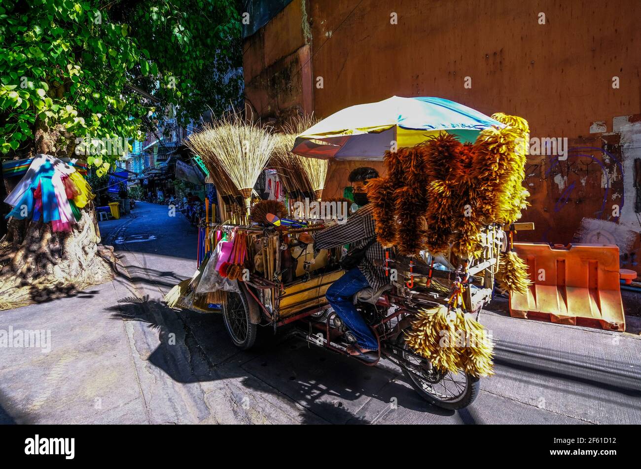 Un venditore di spazzole maschili trasporta i suoi articoli su una moto lungo un vicolo a Talat noi, Bangkok, Thailandia Foto Stock