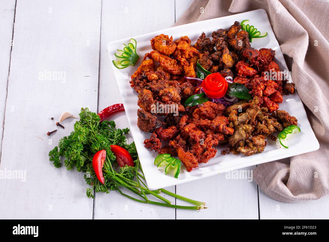 Pakoda di pollo o pakora, tre diversi sapori di pakora disposti in un piatto bianco quadrato e guarnito con pomodoro e cetriolo su uno sfondo bianco Foto Stock