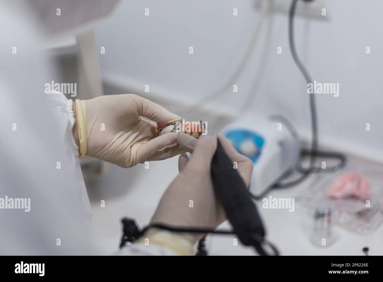 Mani di un tecnico dentale con maschera chirurgica e vetri che lucidano le protesi sulla sua tabella. Concetto di salute Foto Stock