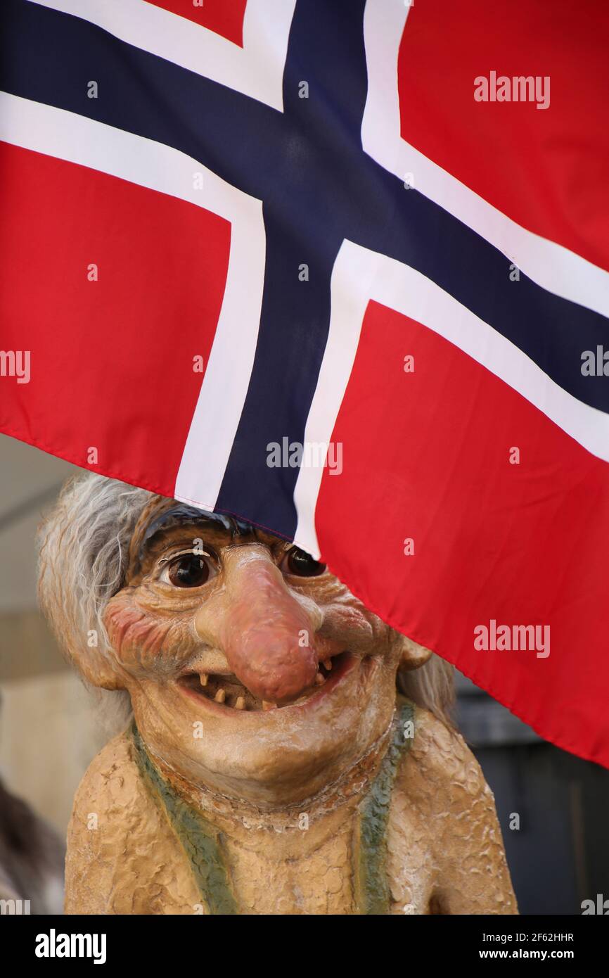 La statua del Troll, tradizionale folklore norvegese, si trova sotto la bandiera rossa, bianca e blu della Norvegia. Foto Stock