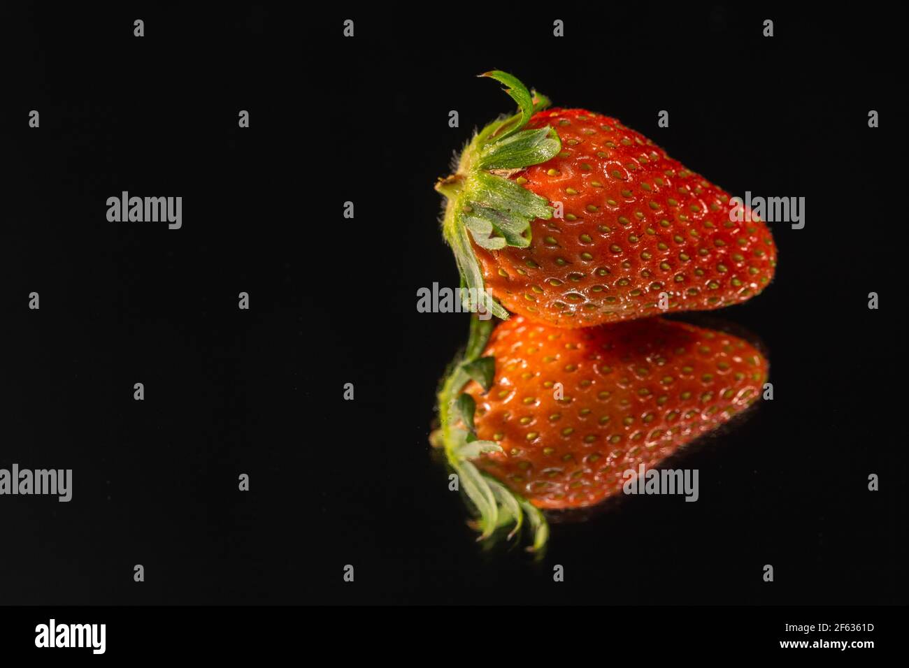 Un dolce frutto rosso morbido con una superficie di semi-borchiata è stato tagliato a metà sullo specchio con uno sfondo nero. Foto Stock