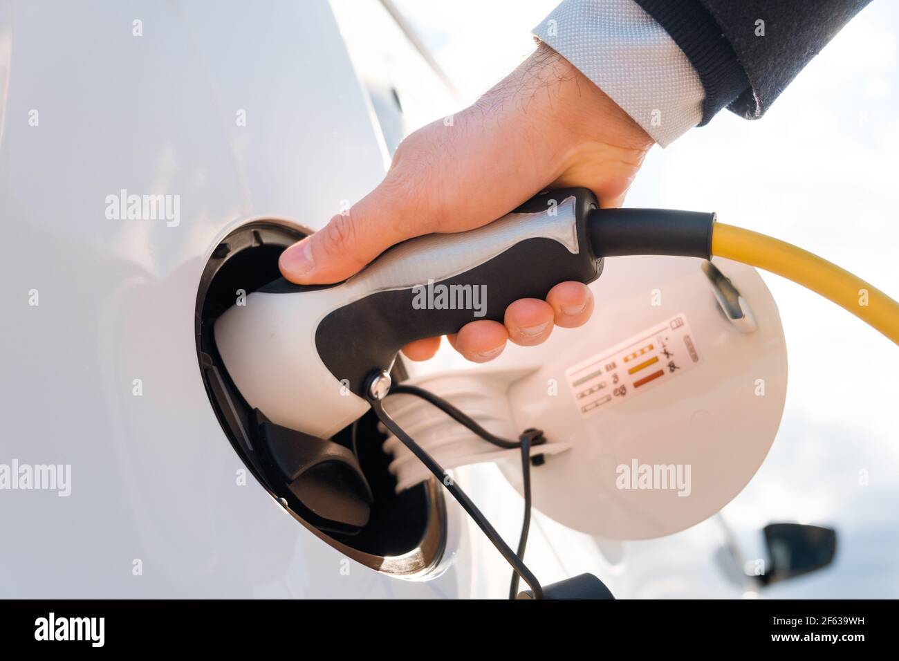 Primo piano uomo nella tuta che collega un alimentatore in un'auto elettrica presso la stazione di ricarica in strada alla luce del sole Foto Stock