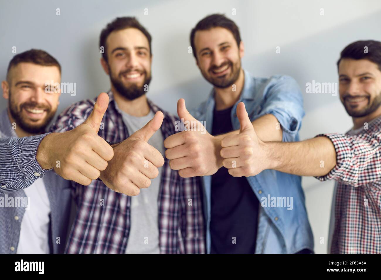Gli amici maschili mostrano piacere e danno un feedback positivo mostrando i pollici contro la parete grigia. Foto Stock