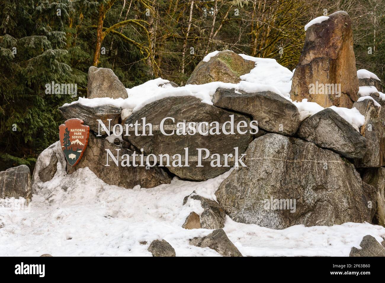 Cartello all'ingresso del North Cascades National Park di Washington State con neve intorno alla struttura rocciosa lungo la strada statale 20 Foto Stock