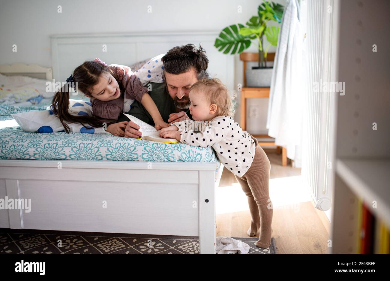 Padre con due piccole figlie che si divertono a letto a casa. Foto Stock