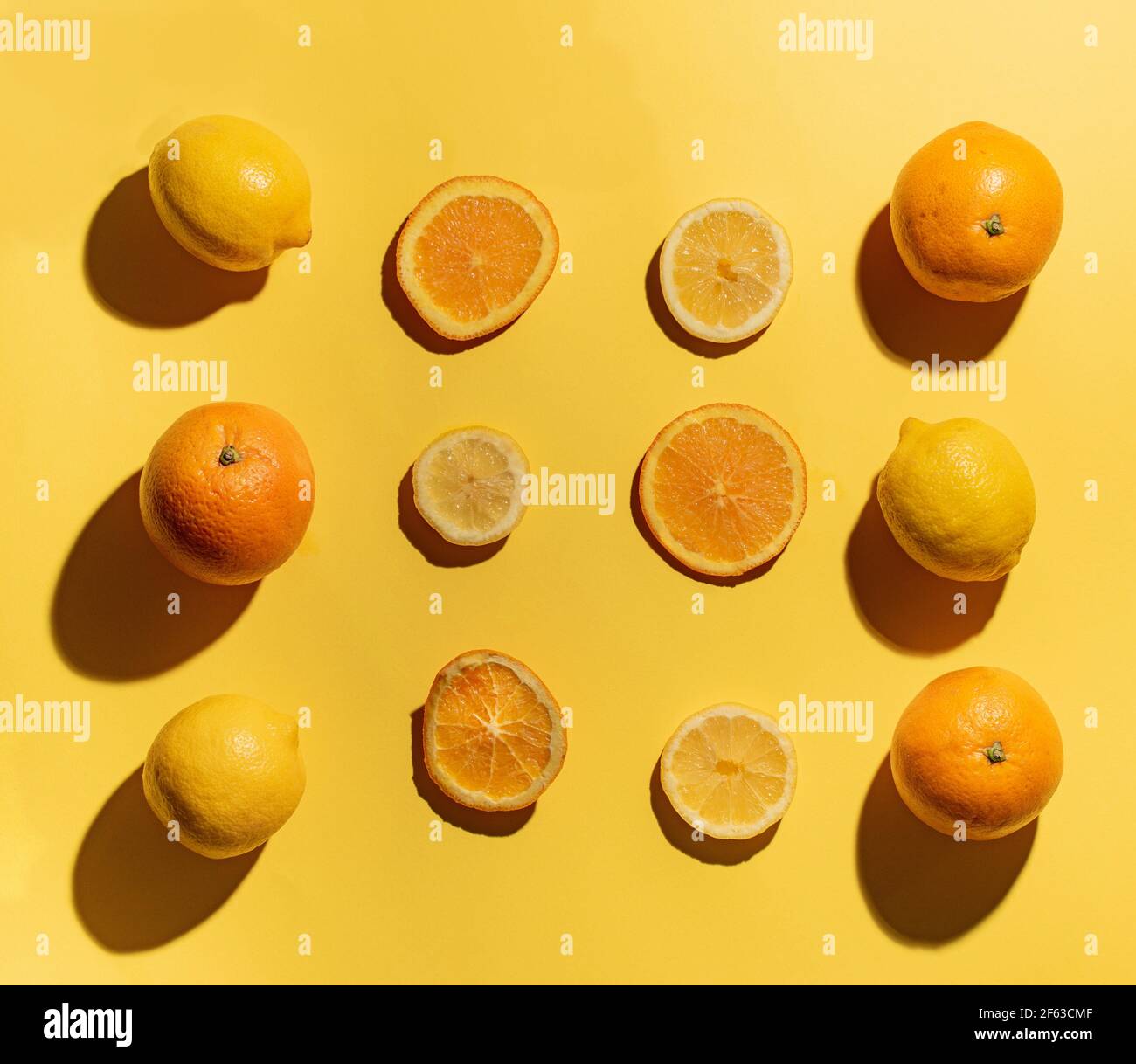 Arance e fette di limone su sfondo giallo con tre limoni e tre arance sui lati Foto Stock