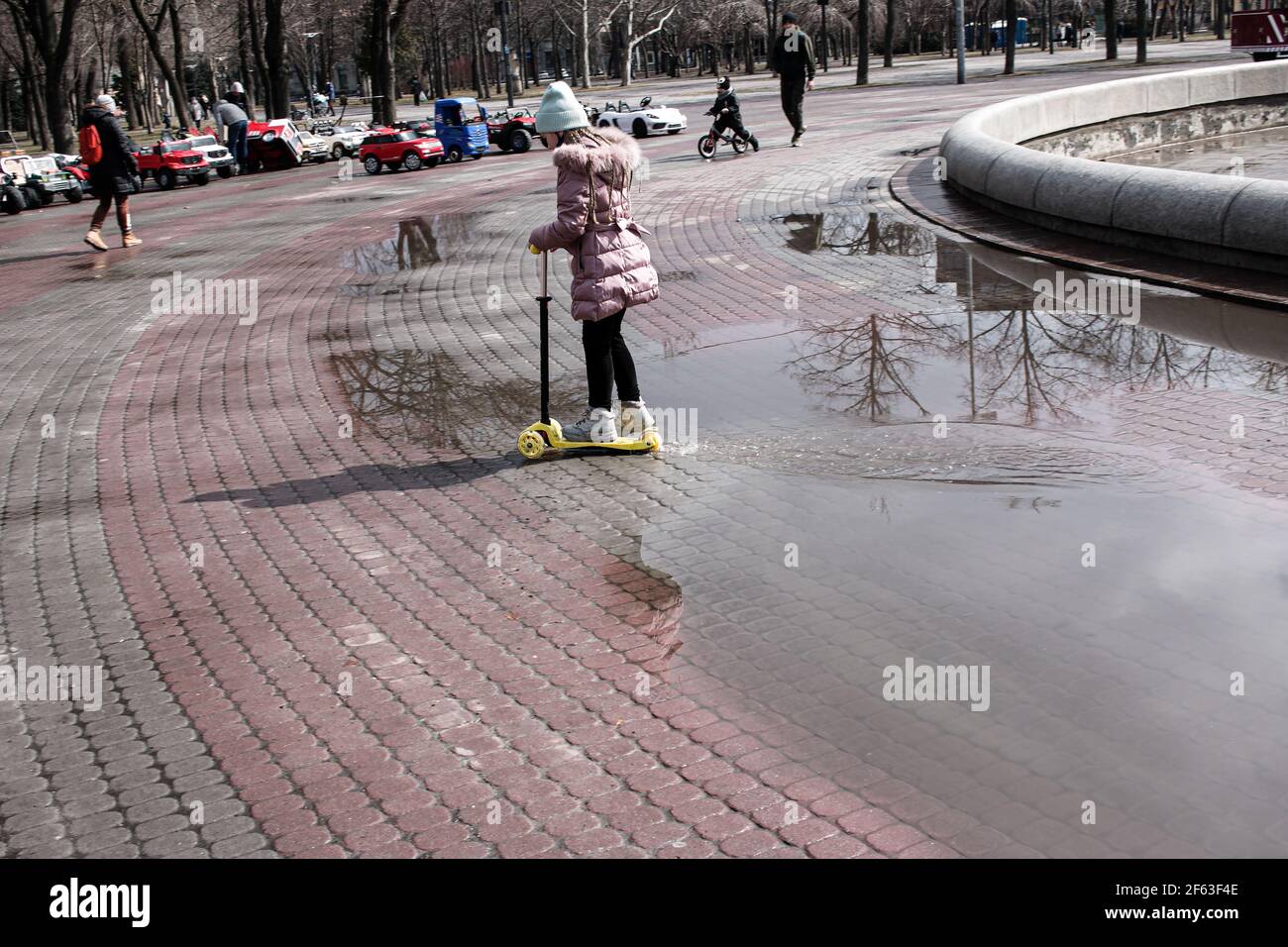 Dnepropetrovsk, Ucraina - 03.21.2021: Genitori e bambini camminano nel parco dopo la pioggia. I riflessi nelle pudddle sono visibili al sole. Foto Stock