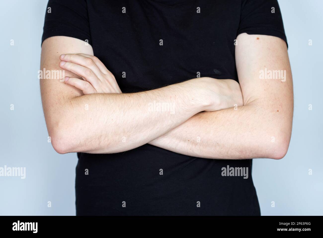 Uomo in una t-shirt nera con le mani incrociate che guardano la macchina fotografica. Isolato su sfondo grigio, foto ritagliata senza testa. Foto Stock