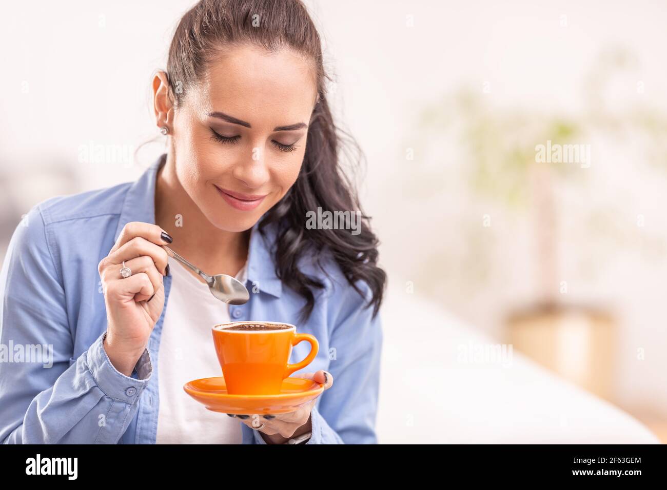 Bella donna odore di caffè fresco da una tazza arancione. Foto Stock