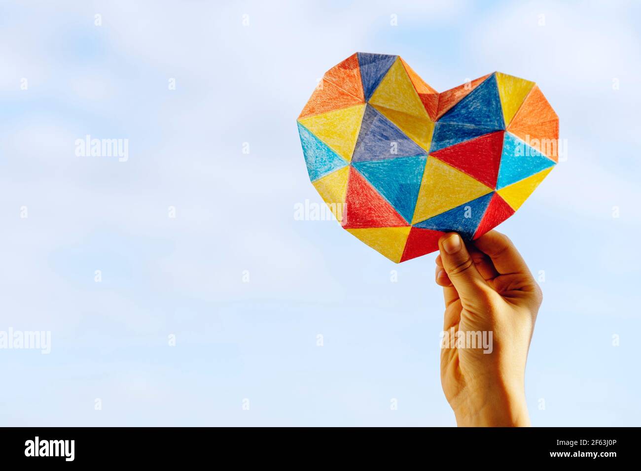 Le mani del bambino tengono il cuore colorato sopra lo sfondo blu del cielo. Concetto di giorno di consapevolezza autismo mondiale Foto Stock