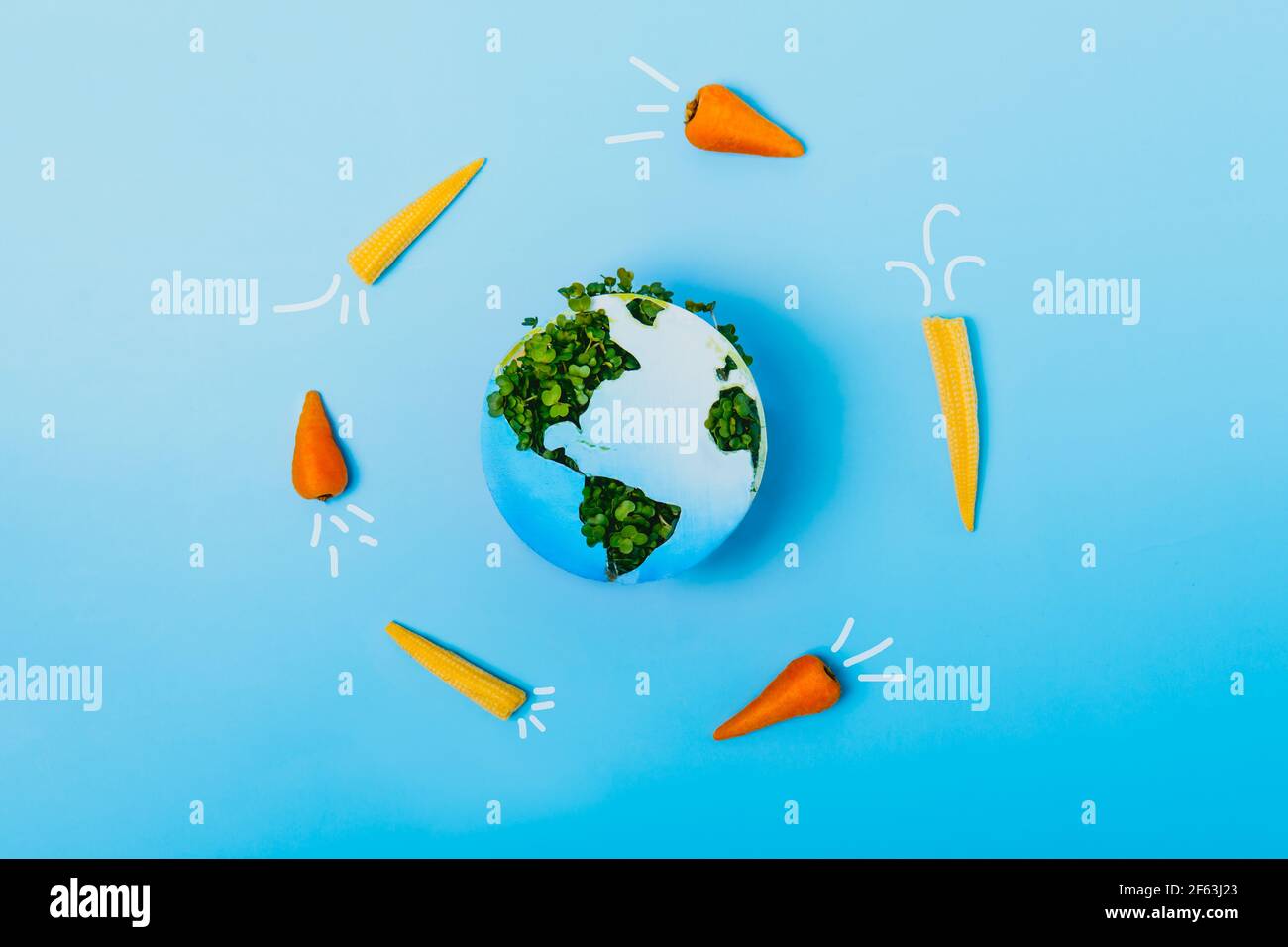 Il veganismo creativo e il concetto del giorno della Terra. Razzi di carote e mais che volano intorno al pianeta Terra. Modello terrestre in carta e verde fresco Foto Stock