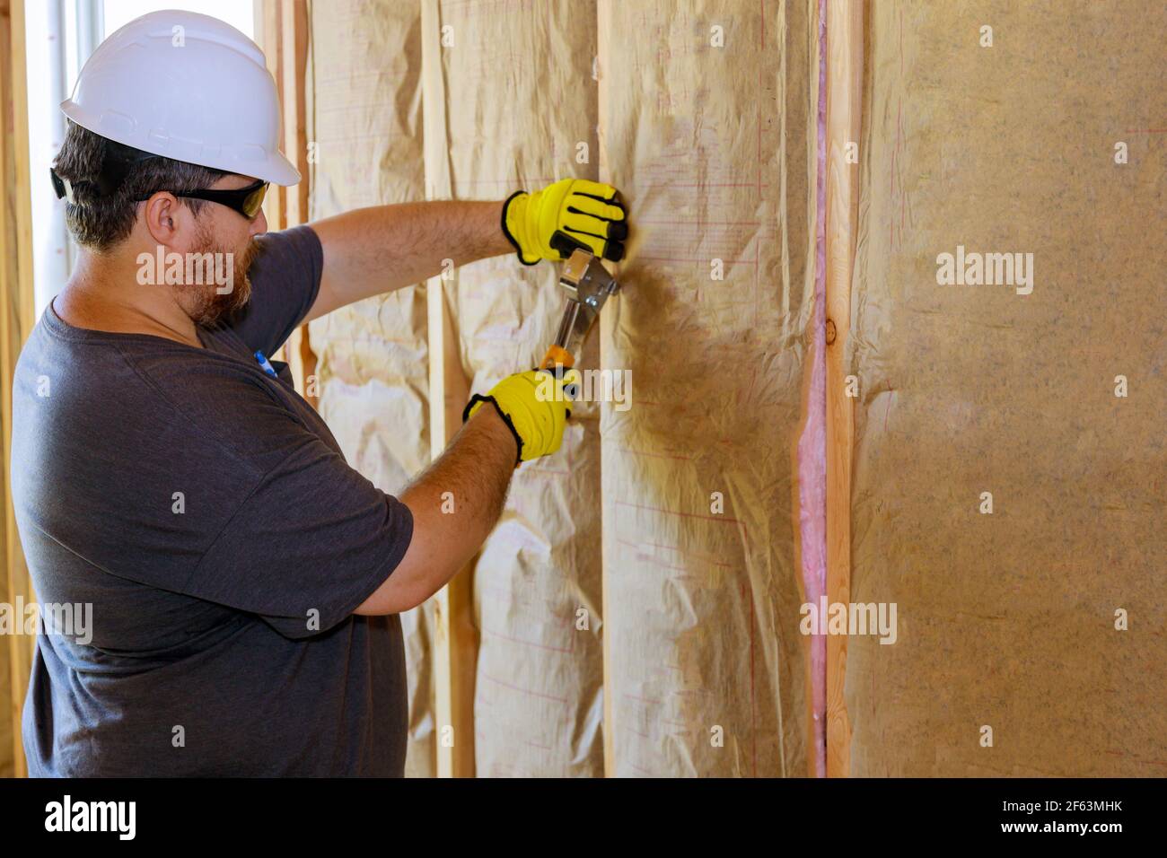 Uomo che installa lo strato di isolamento termico sotto la parete usando lana minerale con fibra di vetro fredda soft focus Foto Stock