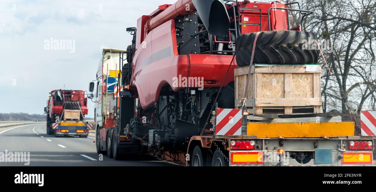 Molti autocarri industriali pesanti con piattaforma di trasporto semirimorchio smontata mietitrebbia su strada pubblica al tramonto o. alba Foto Stock