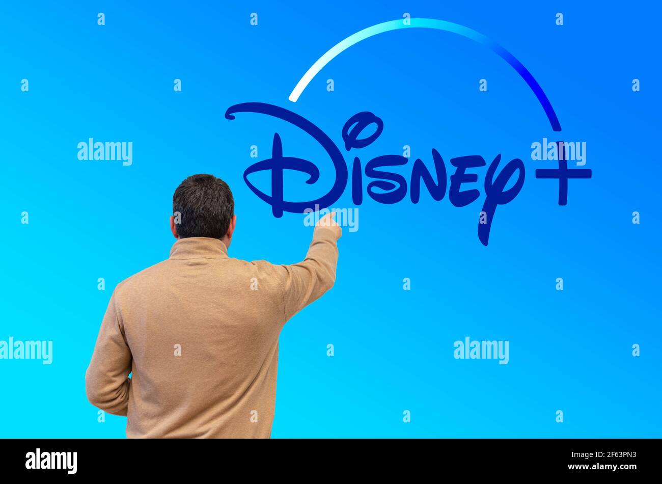 BURGOS, SPAGNA - 29 marzo 2021: Uomo che punta verso uno schermo blu con il dito sul logo del nuovo canale televisivo online chiamato Disney Plus for Foto Stock