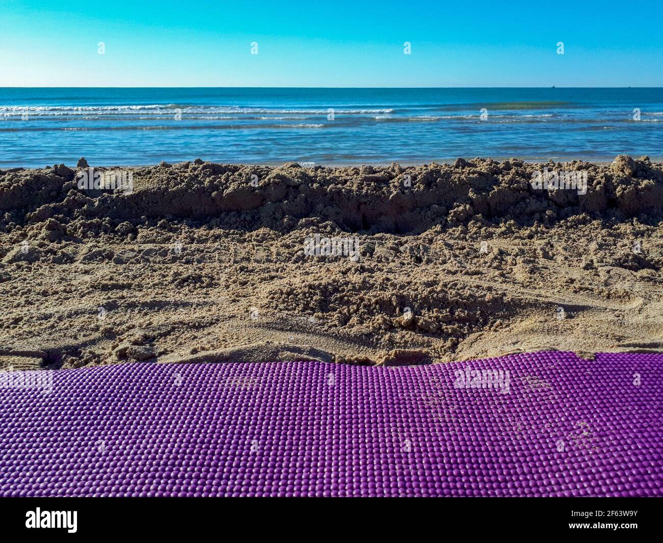 Una foto in primo piano di mare e spiaggia sabbiosa, tappeto yoga sulla sabbia. Yoga in spiaggia per uno stile di vita sano Foto Stock