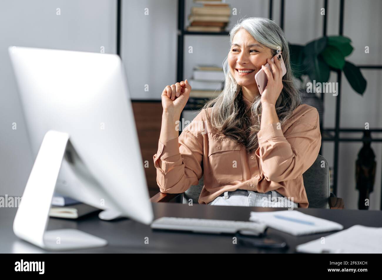 Sicuro di successo bella donna asiatica con capelli grigi senior, leader aziendale, manager, lavorare in ufficio, parlare al telefono con amici o colleghi, guardare via, sorridere Foto Stock