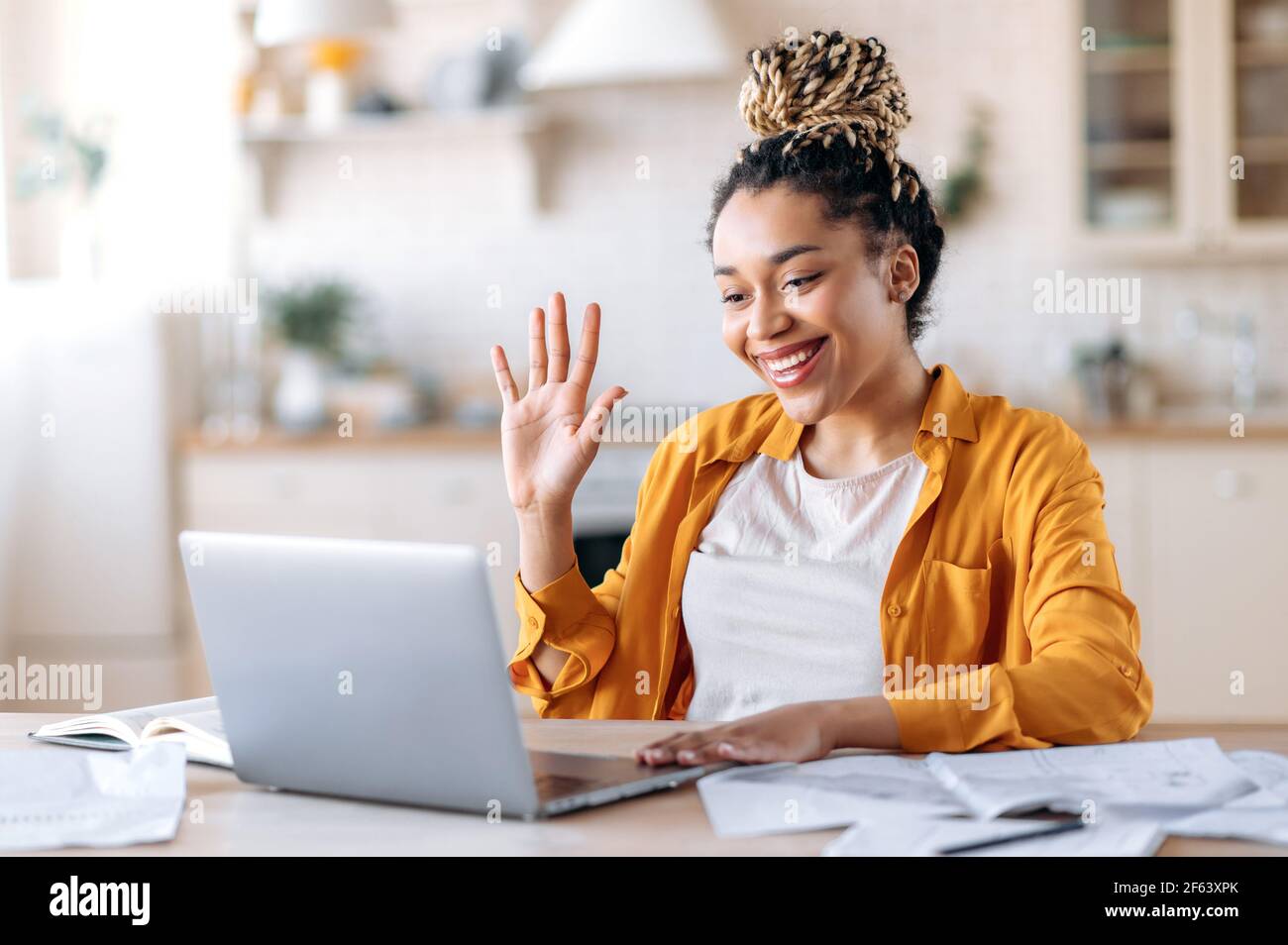 Felice successo bella ragazza afro-americana di stile, studente o freelancer, parlando con videochiamata, incontro online con colleghi o amici, saluto con gesto della mano, sorridente amichevole Foto Stock