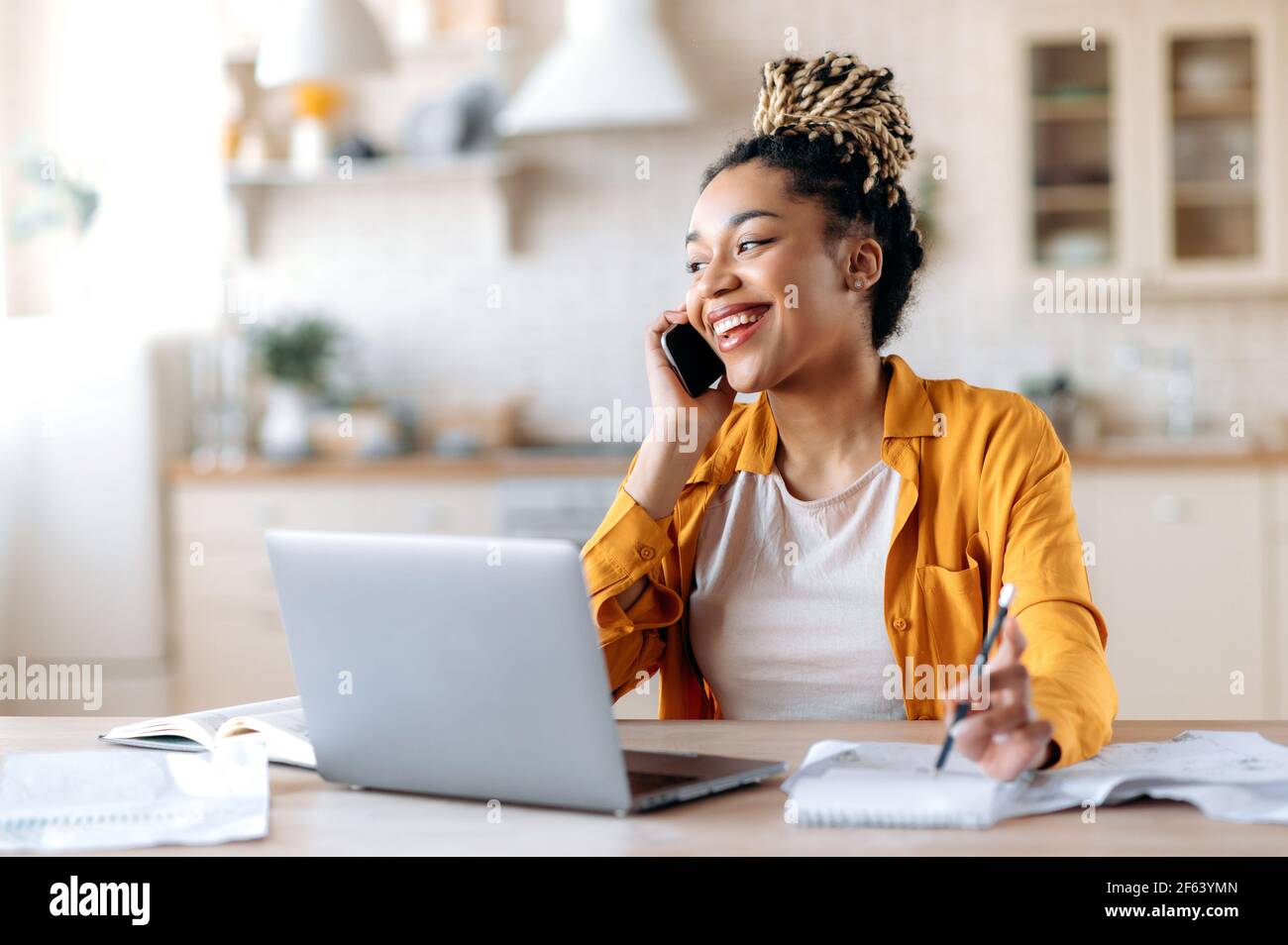 Felice successo occupato giovane donna afro-americana, broker, manager o freelancer che lavorano da remoto, hanno piacevolmente conversazione con il cliente o il dipendente al telefono guardando via sorridente amichevole Foto Stock